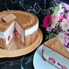 Pyszny sernik lotus z truskawkami, ozdobiony ciasteczkami i posypką. Obok bukiet kwiatów.