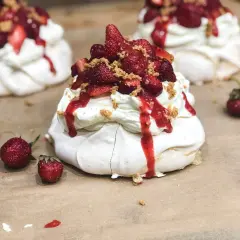 Słodkie mini pavlova z bitą śmietaną, truskawkami i sosem truskawkowym, posypane kruszonką.