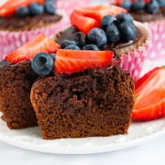Pyszne babeczki brownie z polewą czekoladową, udekorowane truskawkami i borówkami, kuszą swoim wyglądem.