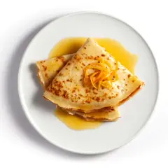 Złożone na pół naleśniki crepes suzette polane pomarańczowym sosem, ozdobione skórką pomarańczową.