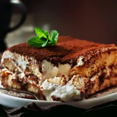 Pyszne tiramisu z mascarpone i śmietaną bez jajek, posypane kakao i ozdobione miętą. Idealne na deser.