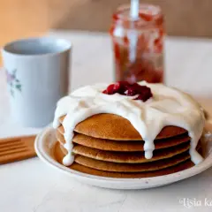 Pyszne pancakes bezglutenowe polane kremowym jogurtem i dżemem, obok kubek i słoiczek z konfiturą.
