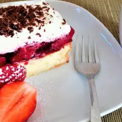 Pyszny biszkopt z serkiem mascarpone i galaretką, udekorowany wiórkami czekolady i podany z truskawkami.