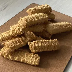 Stos puszystych, chrupiących ciastek z maszynki, ułożonych na brązowej desce.