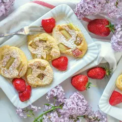 Pyszne racuchy z rabarbarem, posypane cukrem pudrem, podane z truskawkami i bzem.