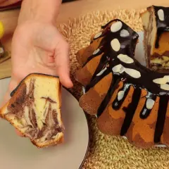 Pyszna babka marmurkowa z polewą czekoladową i migdałami, obok wielkanocne dekoracje.