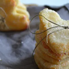 Stos ciasteczek serowych, posypanych cukrem, związanych sznurkiem. Obok widać kolejne, podobne wypieki.