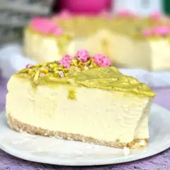 Pyszny sernik w kąpieli wodnej, udekorowany pistacjami i różowymi kwiatkami. Idealny deser na każdą okazję.