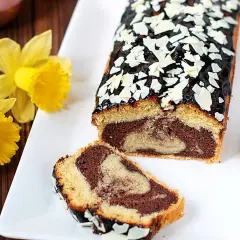 Wilgotna babka marmurkowa z polewą czekoladową i płatkami migdałów, ozdobiona żółtymi żonkilami.