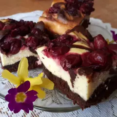 Pyszny sernik z wiśniami na czekoladowym spodzie, udekorowany kwiatami.