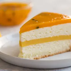 Pyszny tort mango z warstwami musu i galaretki, podany na białym talerzyku. Obok kawałki świeżego mango.