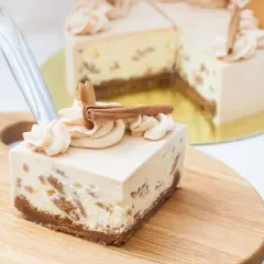 Kawałek sernika Kinder Bueno z kremem i cynamonem na drewnianej desce.