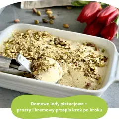 Kremowe lody pistacjowe w białej misce, posypane orzechami. Obok czerwone tulipany.