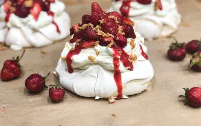Słodkie mini pavlova z bitą śmietaną, truskawkami i sosem truskawkowym, posypane kruszonką.