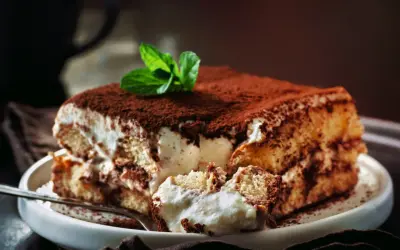Pyszne tiramisu z mascarpone i śmietaną bez jajek, posypane kakao i ozdobione miętą. Idealne na deser.