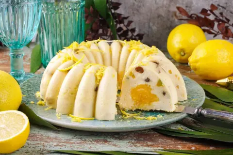 Pyszna babka z owocami, udekorowana skórką cytrynową, prezentuje się apetycznie na talerzu. Obok leżą świeże cytryny.