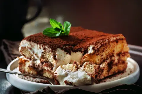 Pyszne tiramisu z mascarpone i śmietaną bez jajek, posypane kakao i ozdobione miętą. Idealne na deser.