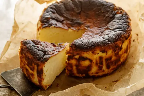 Pyszny, lekko przypieczony sernik belgijski na papierze do pieczenia. Jedna porcja już wycięta, czeka na spróbowanie.