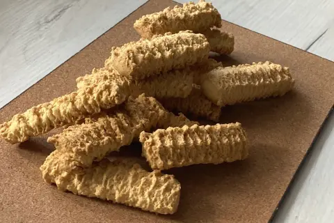 Stos puszystych, chrupiących ciastek z maszynki, ułożonych na brązowej desce.