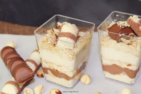 Pyszne deserki Kinder Bueno w pucharkach, warstwowo ułożone z kremem i czekoladą, posypane orzechami.