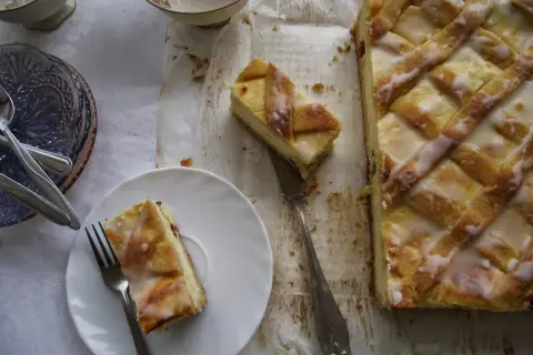 Pyszny sernik krakowski z kratką z ciasta i lukrem, jeden kawałek na talerzyku, gotowy do degustacji.