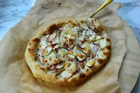 Apetyczna pizza bianca z jabłkami i serem, podana na papierze do pieczenia.