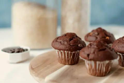 Pyszne muffinki czekoladowe, gotowe do jedzenia. W tle słoiki z cukrem i mąką.