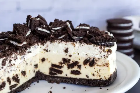 Pyszny sernik oreo z kawałkami ciastek i kremową masą, posypany pokruszonymi oreo.