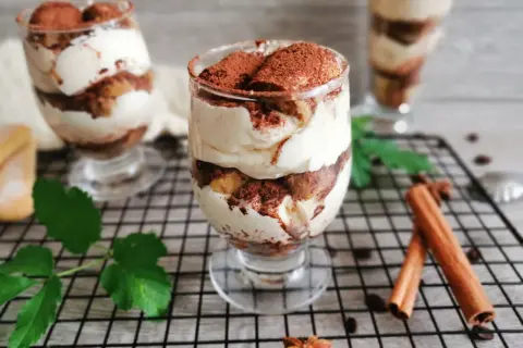 Pyszne tiramisu w pucharkach, warstwowo ułożone z kremem i biszkoptami, posypane kakao. Idealne na deser.