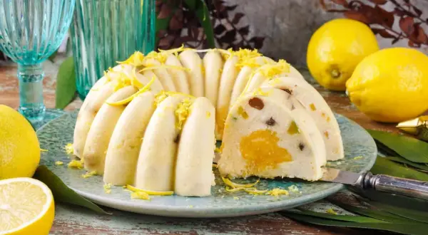 Pyszna babka z owocami, udekorowana skórką cytrynową, prezentuje się apetycznie na talerzu. Obok leżą świeże cytryny.