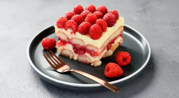 Pyszne tiramisu malinowe z warstwami biszkoptów, kremu i malin, ozdobione świeżymi malinami.