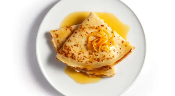 Złożone na pół naleśniki crepes suzette polane pomarańczowym sosem, ozdobione skórką pomarańczową.