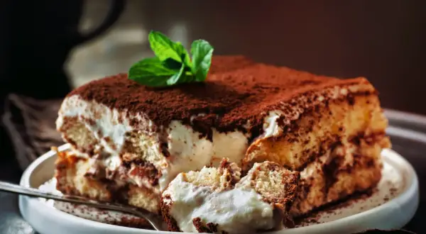 Pyszne tiramisu z mascarpone i śmietaną bez jajek, posypane kakao i ozdobione miętą. Idealne na deser.