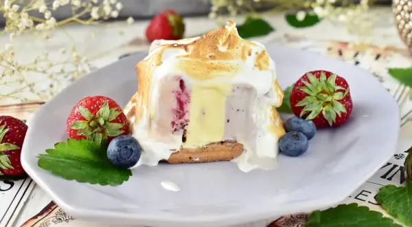Pyszne baked alaska z lodami, owocami i bezą na talerzu.
