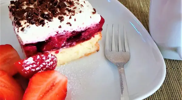 Pyszny biszkopt z serkiem mascarpone i galaretką, udekorowany wiórkami czekolady i podany z truskawkami.