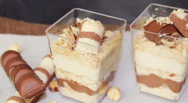 Pyszne deserki Kinder Bueno w pucharkach, warstwowo ułożone z kremem i czekoladą, posypane orzechami.