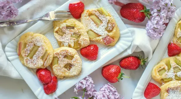 Pyszne racuchy z rabarbarem, posypane cukrem pudrem, podane z truskawkami i bzem.