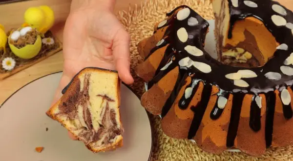 Pyszna babka marmurkowa z polewą czekoladową i migdałami, obok wielkanocne dekoracje.