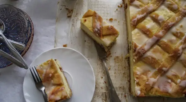 Pyszny sernik krakowski z kratką z ciasta i lukrem, jeden kawałek na talerzyku, gotowy do degustacji.