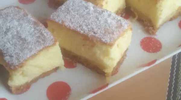 Kawałki puszystego ciasta, posypane cukrem pudrem, wyglądają jak sernik bez sera. Idealne na deser.