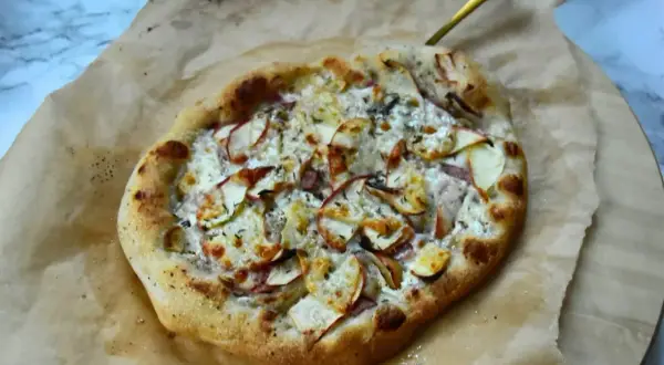 Apetyczna pizza bianca z jabłkami i serem, podana na papierze do pieczenia.