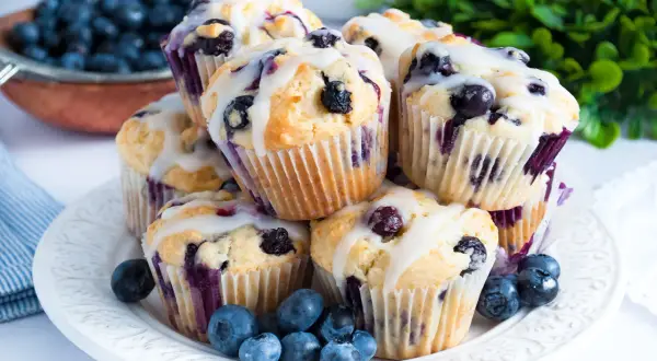 Stos pysznych muffinek z borówkami, polanych lukrem, ozdobionych świeżymi borówkami.