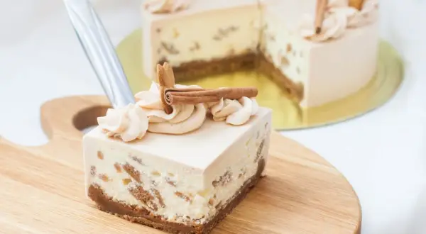 Kawałek sernika Kinder Bueno z kremem i cynamonem na drewnianej desce.