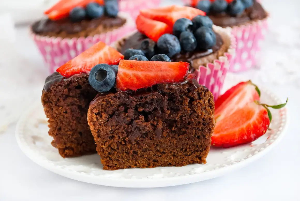 Pyszne babeczki brownie z polewą czekoladową, udekorowane truskawkami i borówkami, kuszą swoim wyglądem.