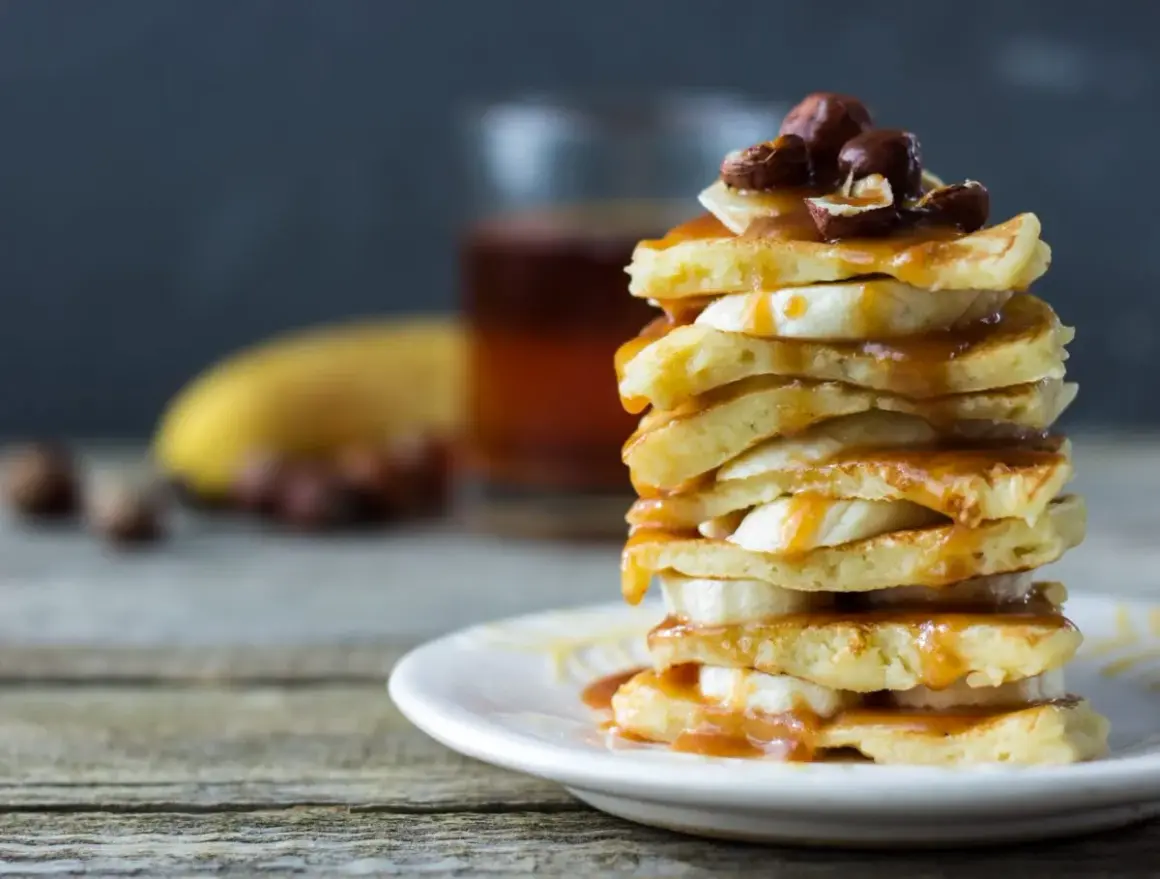 Stos placków bananowych polanych karmelem, ozdobiony orzechami. Idealne na śniadanie.