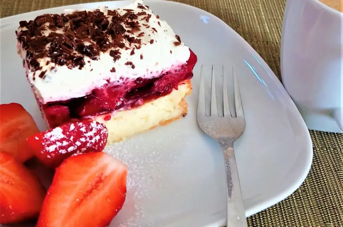Pyszny biszkopt z serkiem mascarpone i galaretką, udekorowany wiórkami czekolady i podany z truskawkami.