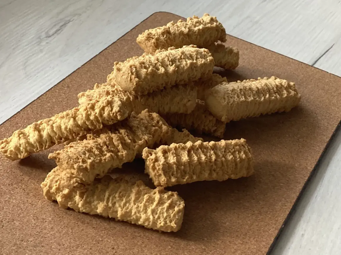Stos puszystych, chrupiących ciastek z maszynki, ułożonych na brązowej desce.