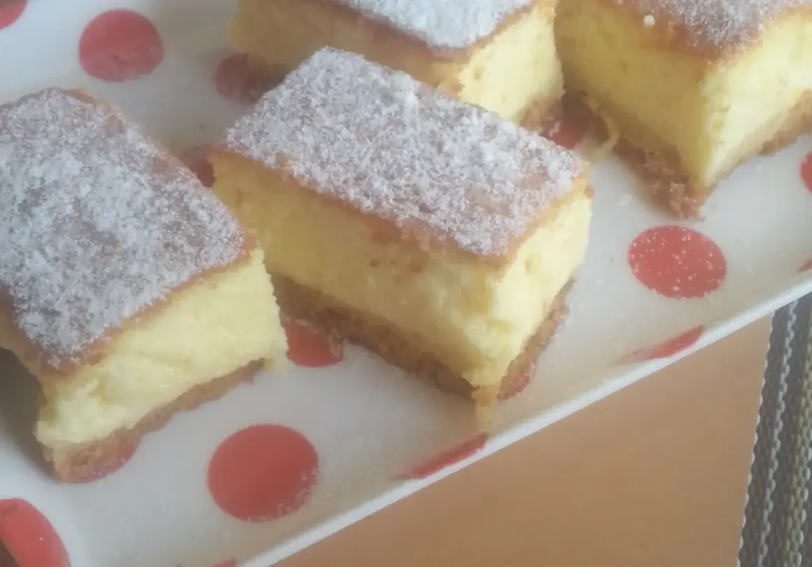 Kawałki puszystego ciasta, posypane cukrem pudrem, wyglądają jak sernik bez sera. Idealne na deser.