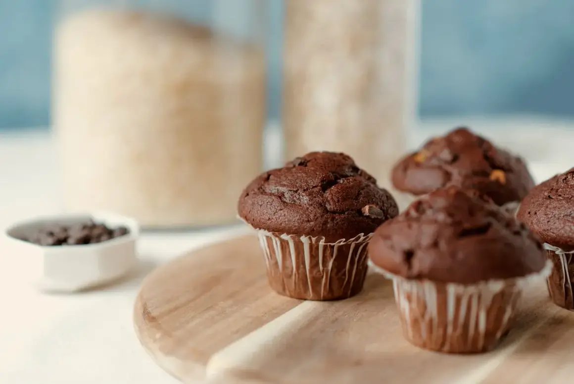 Pyszne muffinki czekoladowe, gotowe do jedzenia. W tle słoiki z cukrem i mąką.