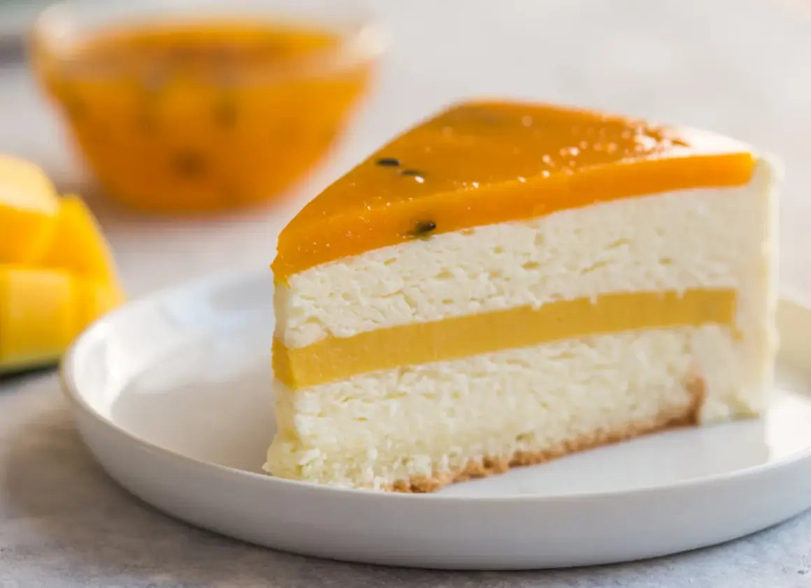 Pyszny tort mango z warstwami musu i galaretki, podany na białym talerzyku. Obok kawałki świeżego mango.